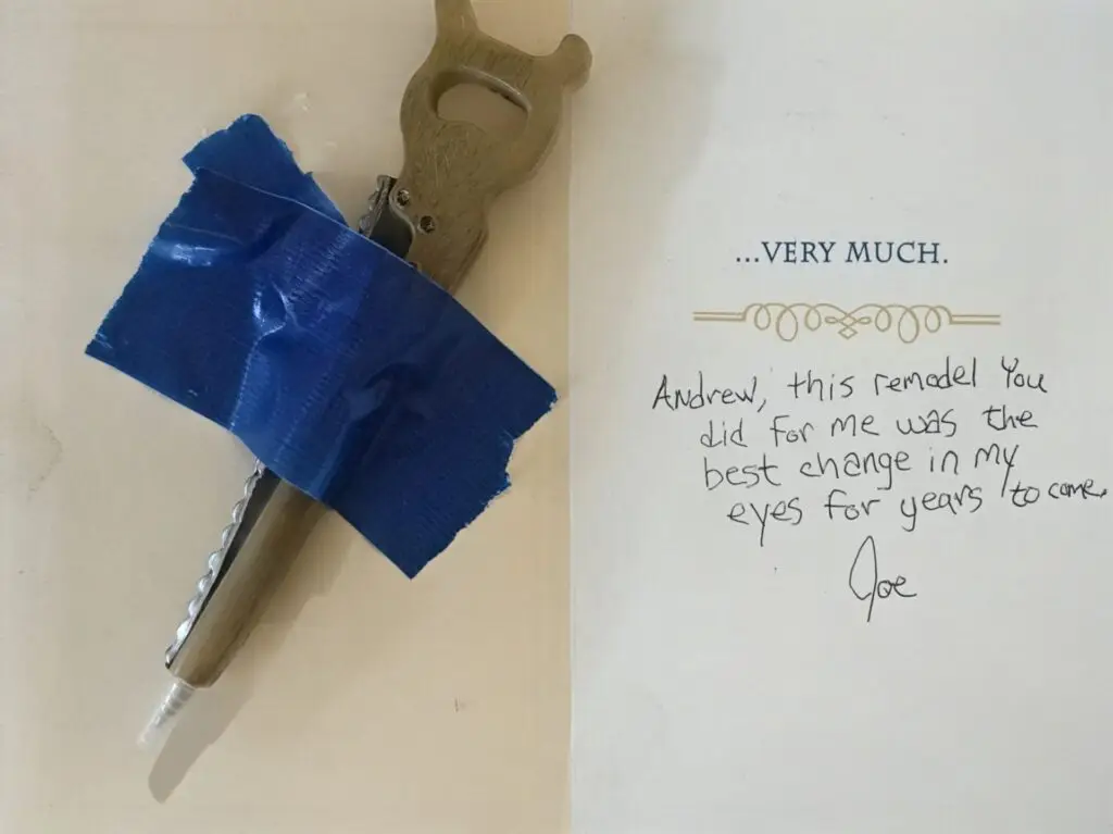 Handwritten testimonial card from a client thanking Andrew at Hetland Home Improvement for a remodel, featuring a novelty hand-saw pen taped to the note.