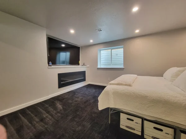 Finished basement bedroom with a flush-mounted electric fireplace and TV in Missoula.