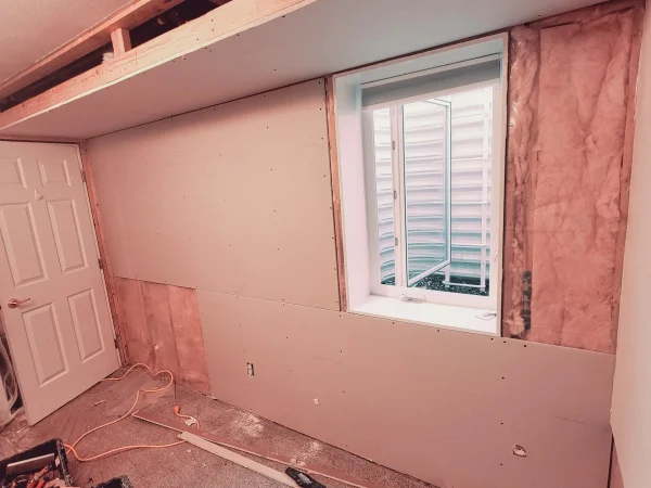 Hanging new drywall over fiberglass insulation in a Missoula basement restoration.