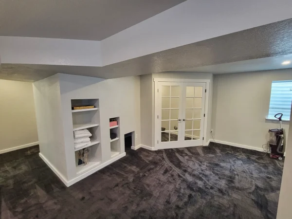 Finished basement room with white French doors and custom built-in shelving in Missoula.