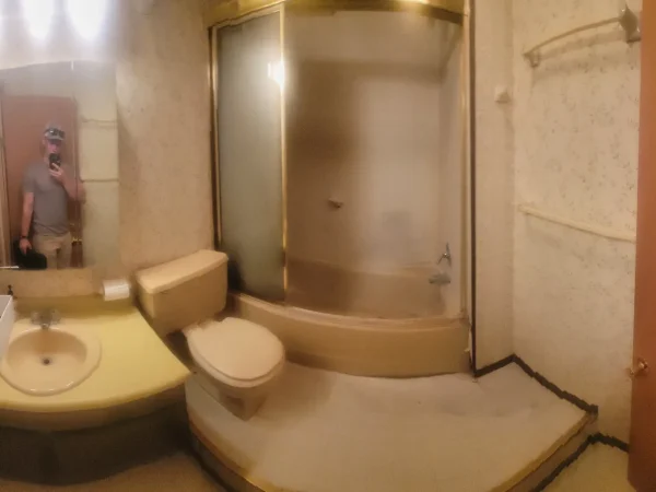 Old bathroom with peeling wallpaper and an outdated tub