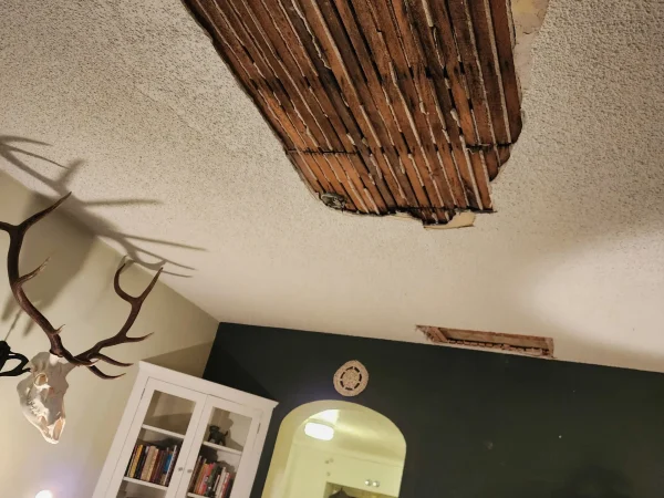 Large hole in a popcorn ceiling exposing original wood lath after water damage.